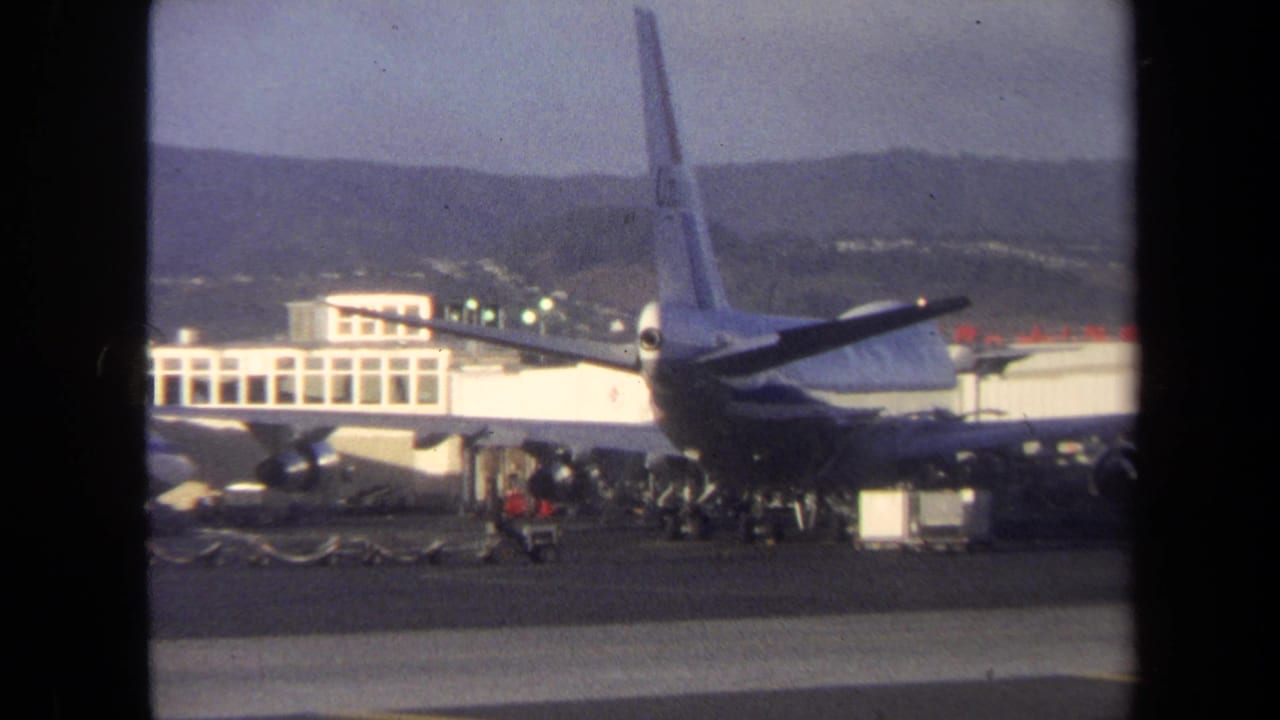 1970 Washington, DC airport view of a large commercial jet at a terminal, with ramp workers and luggage equipment below the wing.
