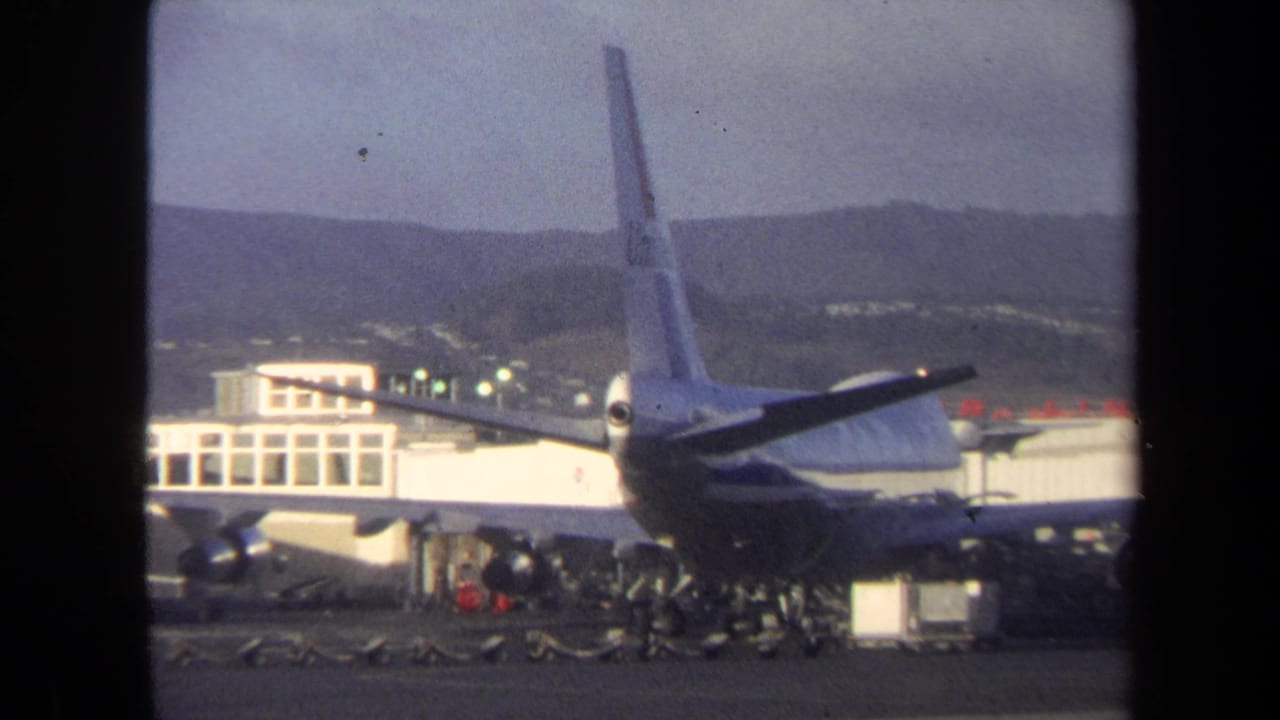 Jet tail and wing beside an airport terminal with ground activity below.