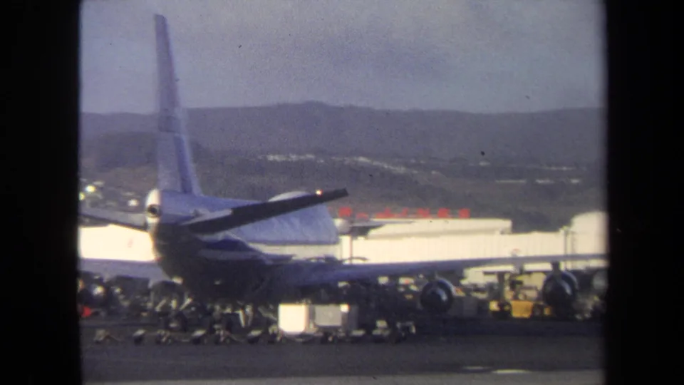 Rear view of a commercial jet at a 1970 Washington, DC airport terminal, with baggage carts and service gear clustered on the apron.
