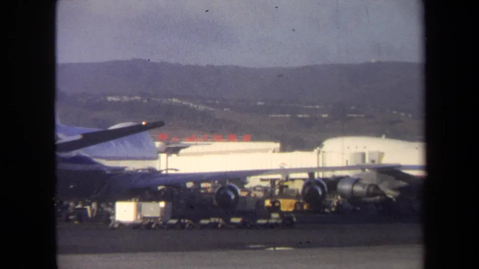 1970 Washington, DC tarmac view showing part of a parked jet, visible engines, baggage carts, service vehicles, and terminal buildings.