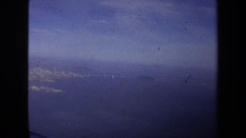 1970 8mm home-movie frame from a Washington DC travel reel showing blue sky and distant terrain through an airplane window.