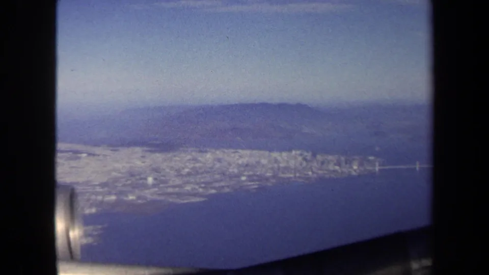The 8mm aerial view looks down over a coastal city and water, with the aircraft engine partly visible at the lower left.