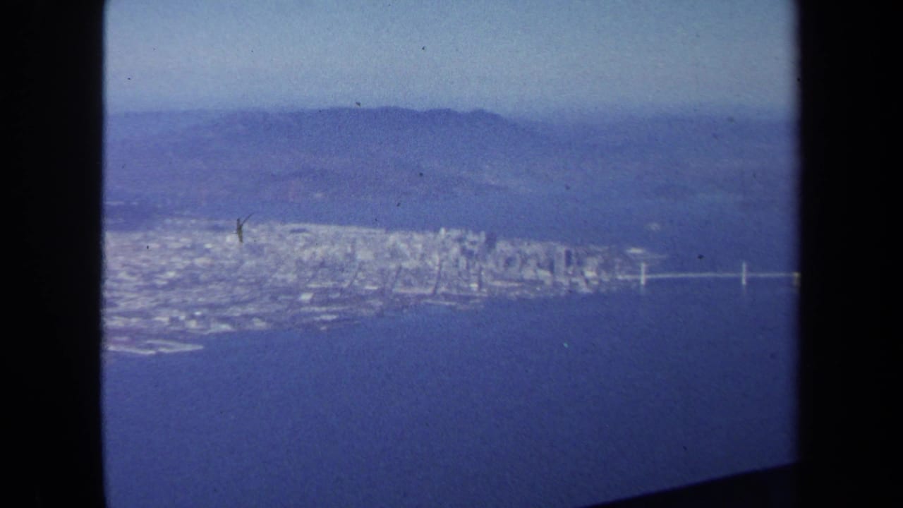 1970 8mm aerial view, identified by metadata as Washington DC, showing a waterfront city, bridge, haze, and aircraft window edges.