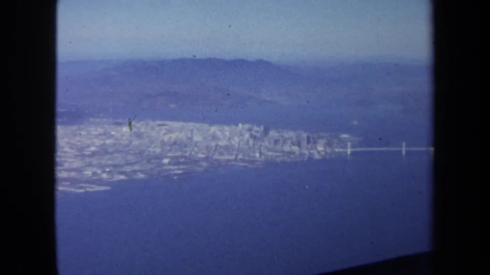 1970 8mm aerial view, identified by metadata as Washington DC, showing a waterfront city, bridge, haze, and aircraft window edges.