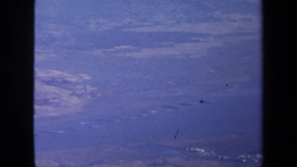 Final 1970 aerial frame showing a broad blue water view, faint shoreline, distant land, and visible 8mm dust marks.