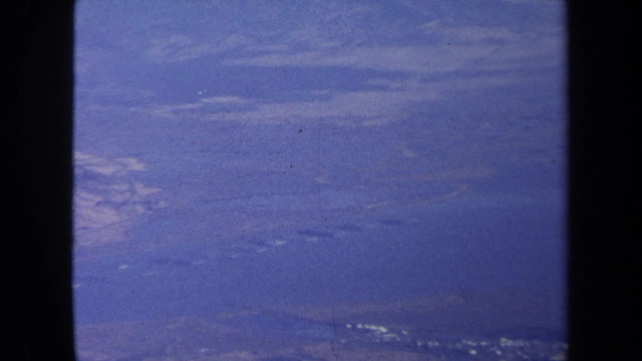 1970 home-movie aerial view over distant terrain near Washington DC, with hazy sky, blue color cast, and dark frame borders.