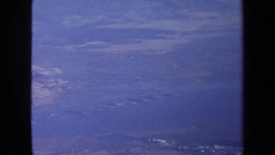 1970 home-movie aerial view over distant terrain near Washington DC, with hazy sky, blue color cast, and dark frame borders.