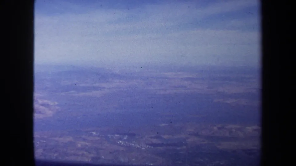 1970 Washington DC travel footage shows a soft blue aerial view of land patterns, clouds, and dark scan borders.