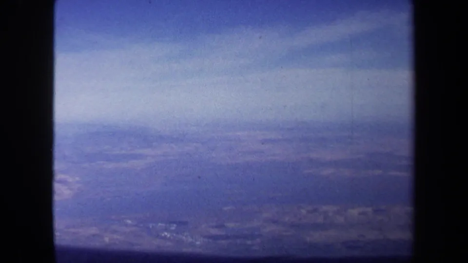 Blue-toned 1970 home-movie frame of distant terrain near Washington DC, with haze, grain, and a dark side border.