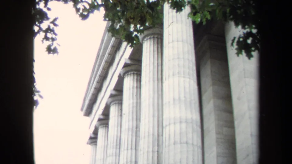 1970 Washington, DC 8mm frame showing tall neoclassical columns viewed from below with dark tree branches at the top.