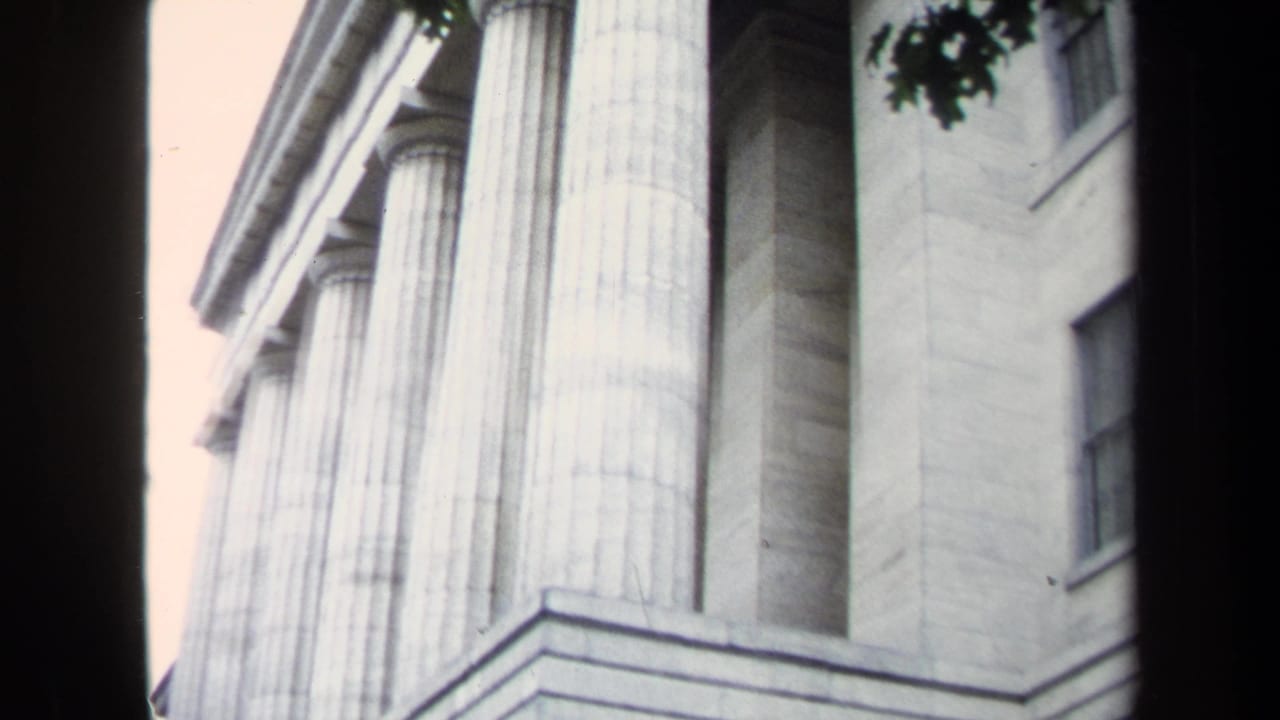1970 Washington, DC home-movie frame looking up at a neoclassical stone facade with large fluted columns and entablature lines.