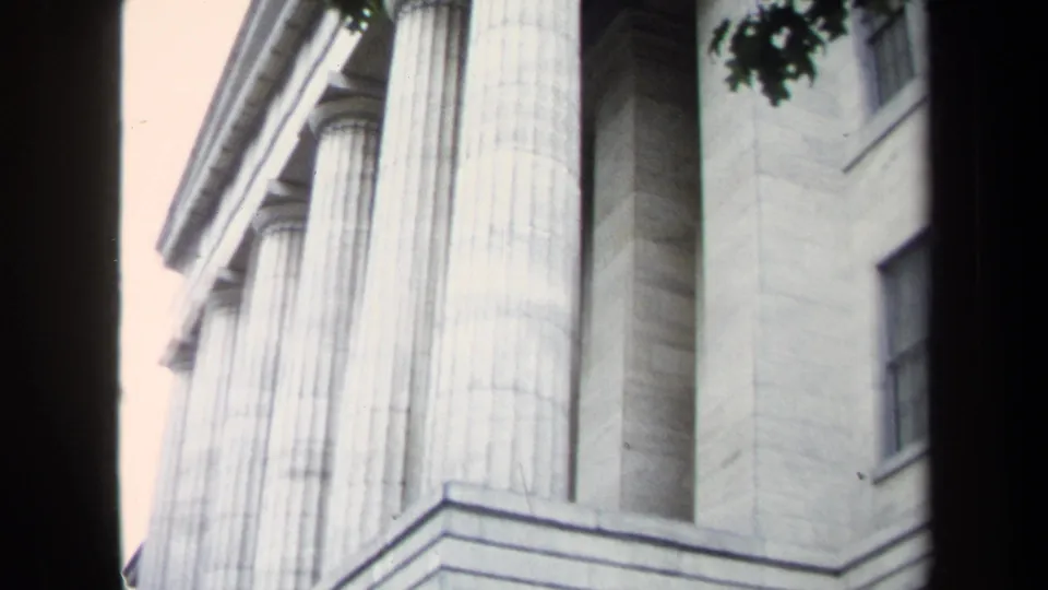 1970 Washington, DC home-movie frame looking up at a neoclassical stone facade with large fluted columns and entablature lines.