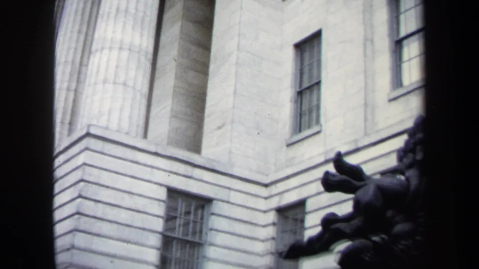 1970 Washington, DC 8mm frame showing a neoclassical facade with windows and the partial silhouette of a dark rearing-horse sculpture.