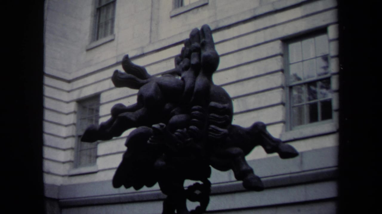 1970 Washington DC home-movie frame with a dark modern sculpture set against a pale formal building exterior and windows.