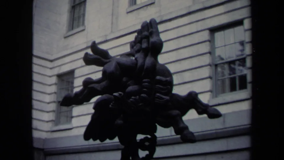 1970 Washington DC home-movie frame with a dark modern sculpture set against a pale formal building exterior and windows.