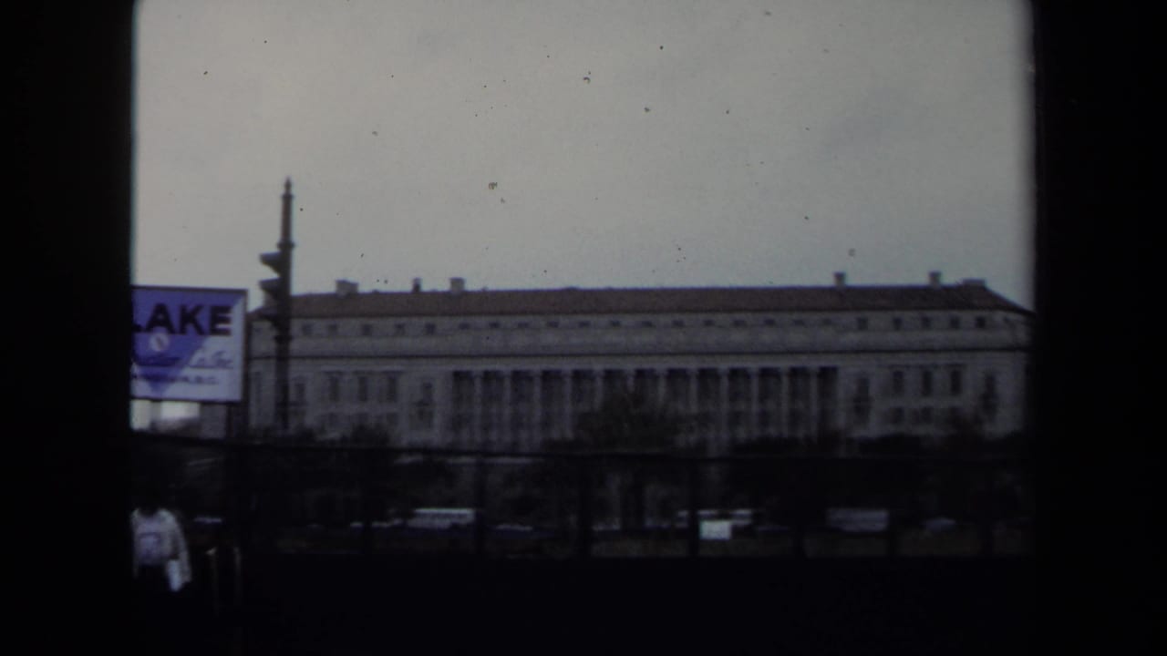 1970 Washington DC street view from a moving vehicle, showing a large classical government-style building and a Blake Construction Co. sign.
