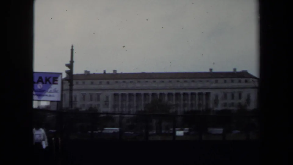 1970 Washington DC street view from a moving vehicle, showing a large classical government-style building and a Blake Construction Co. sign.