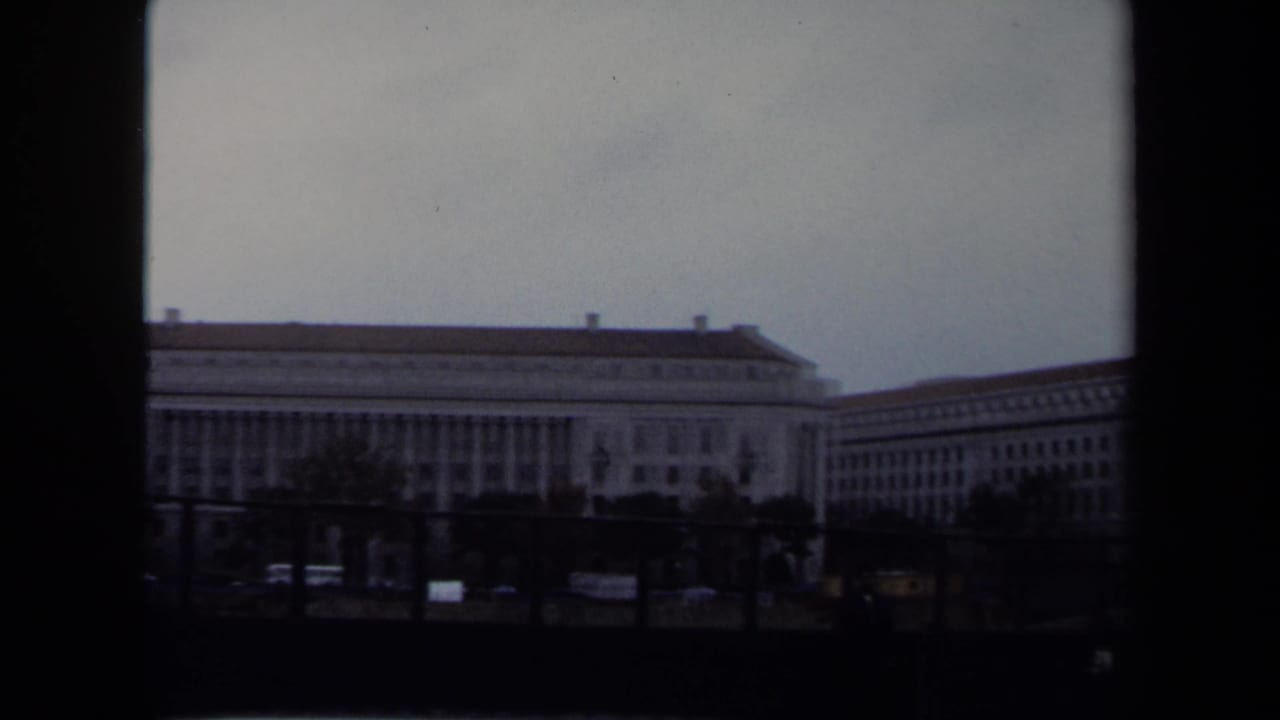 Long stone government-style building viewed across a street under an overcast sky.
