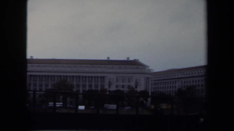 1970 Washington DC moving-vehicle view of a long classical civic building with columns and street activity in the foreground.