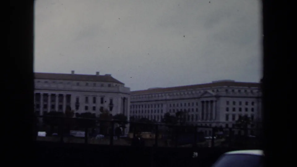 1970 Washington DC street-level view showing large government-style buildings, parked or moving vehicles, and dark 8mm frame edges.
