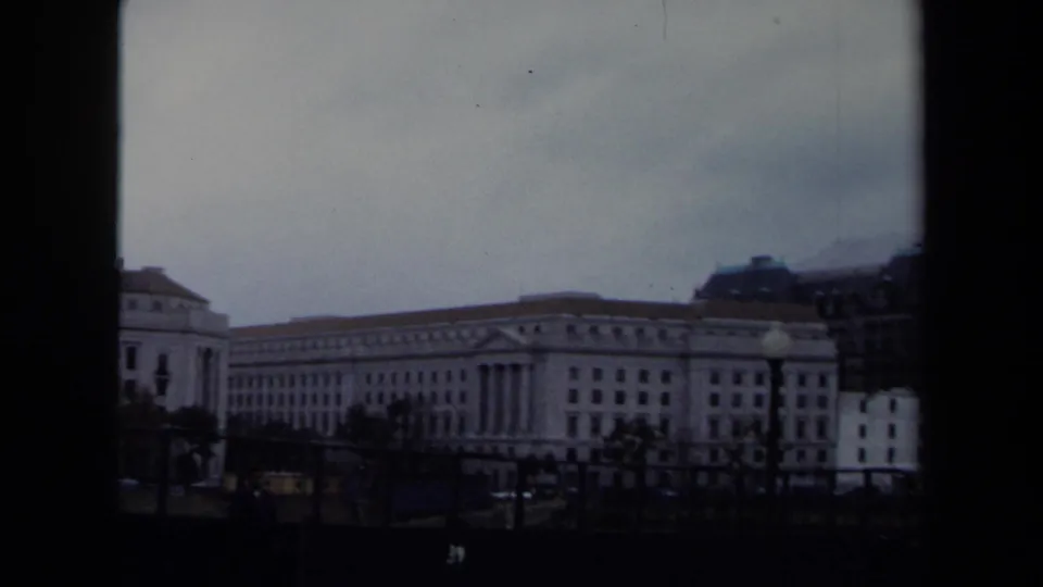 1970 Washington DC moving view of a large civic building with a columned section, distant vehicles, and muted 8mm color.