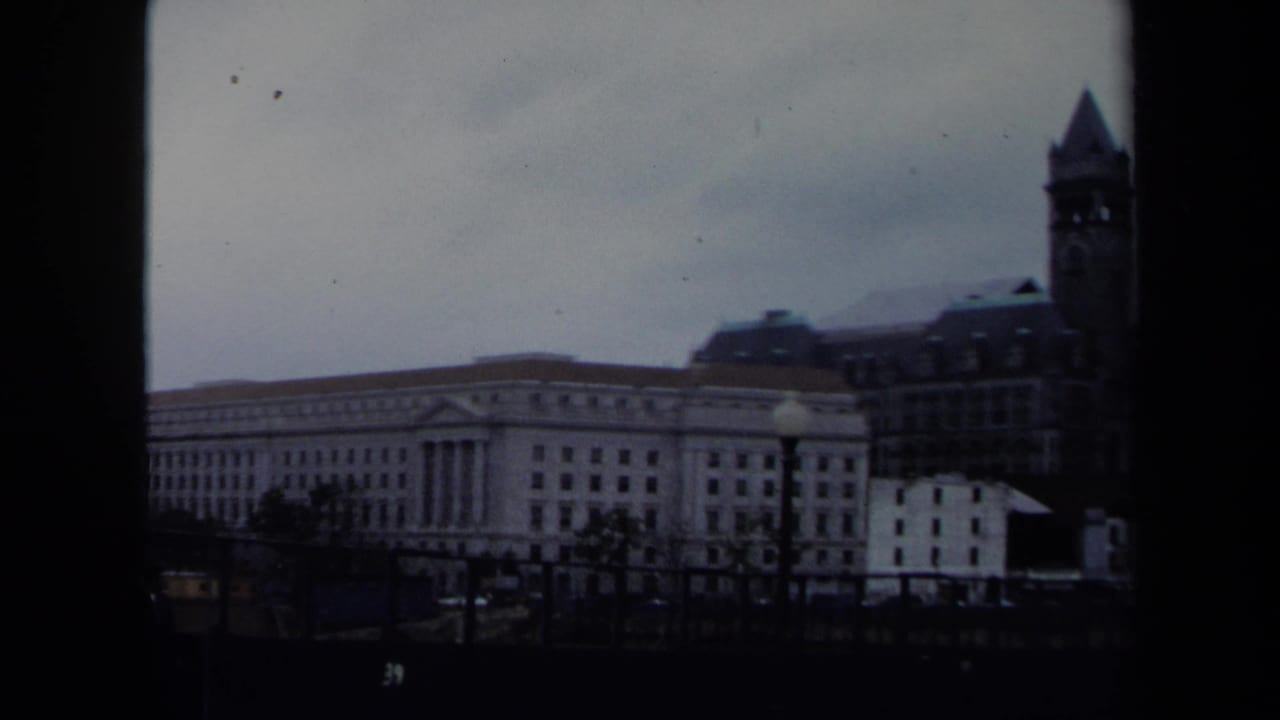 1970 8mm Washington, DC view of downtown buildings, railings, street lamps, and a pointed tower at the right edge.