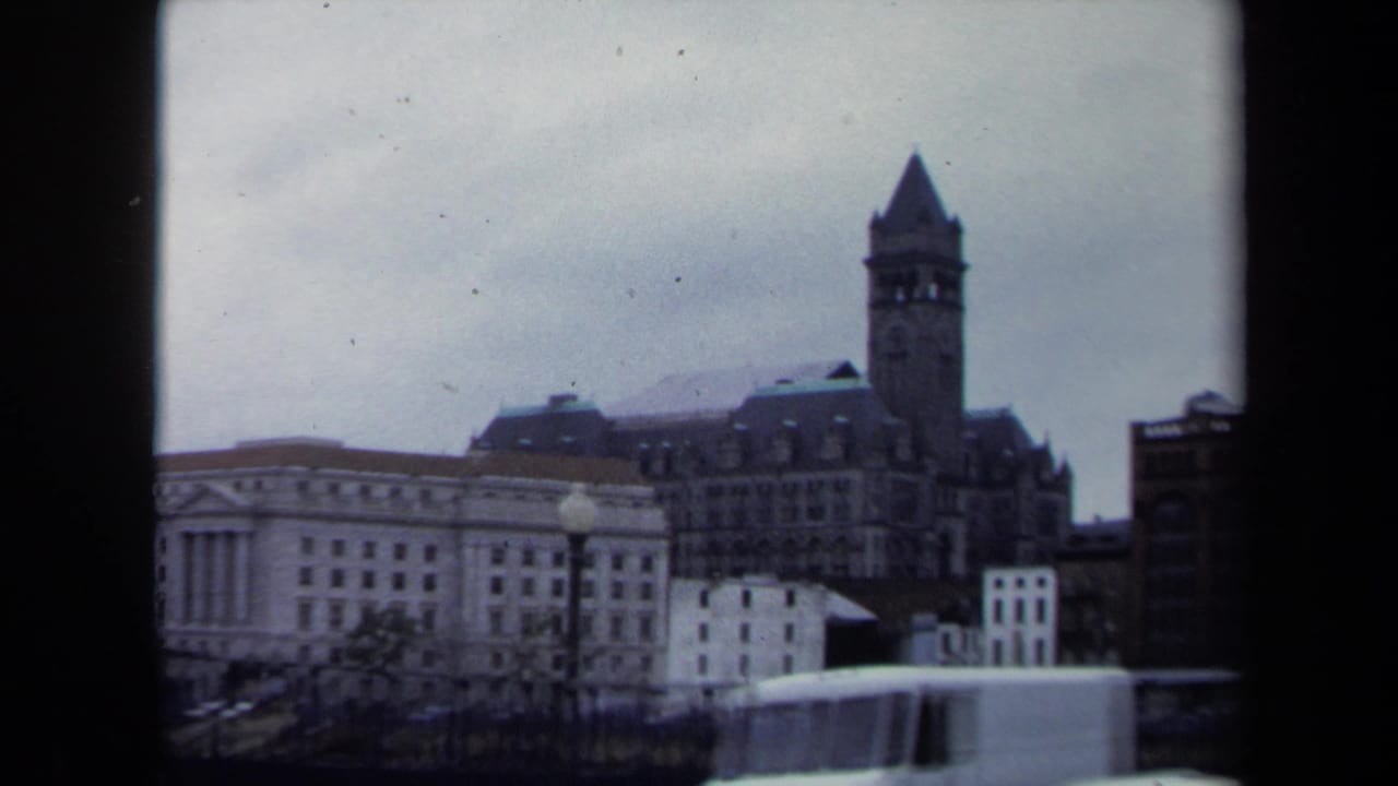1970 8mm Washington, DC frame with a pointed clock tower, downtown facades, street lamps, and a white truck moving across the lower edge.