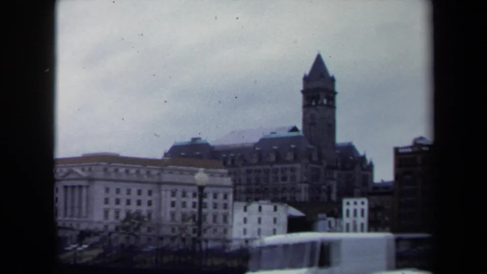 1970 8mm Washington, DC frame with a pointed clock tower, downtown facades, street lamps, and a white truck moving across the lower edge.
