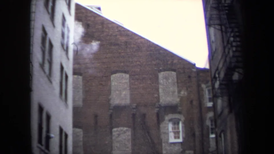 Washington, DC alley view with a brick wall, boarded windows, adjacent building walls, and light smoke or steam near the roofline.