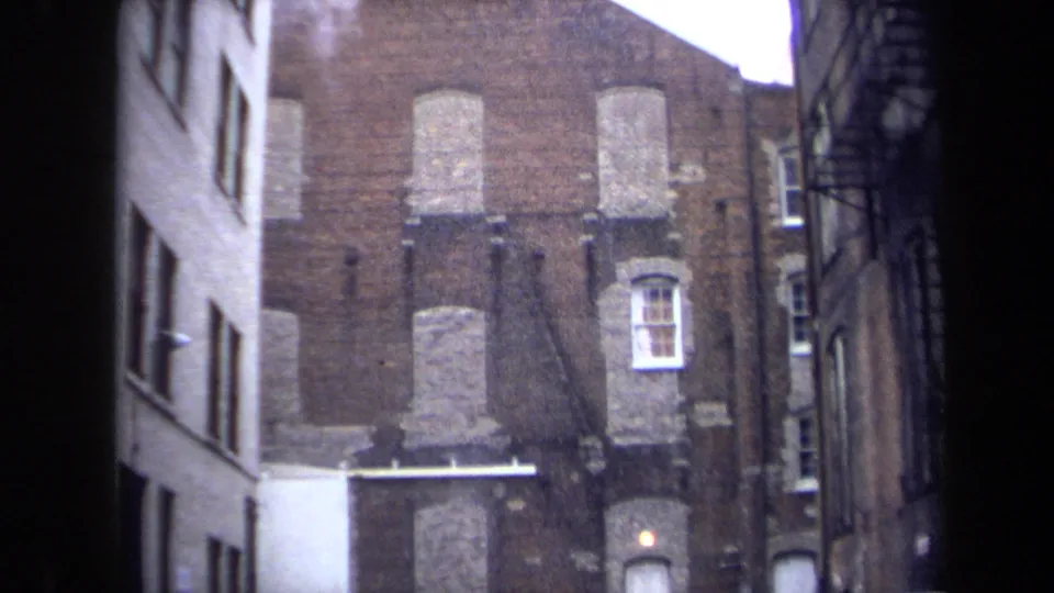 1970 Washington, DC alley frame showing boarded brick openings, a light awning or ledge, and parked cars below.