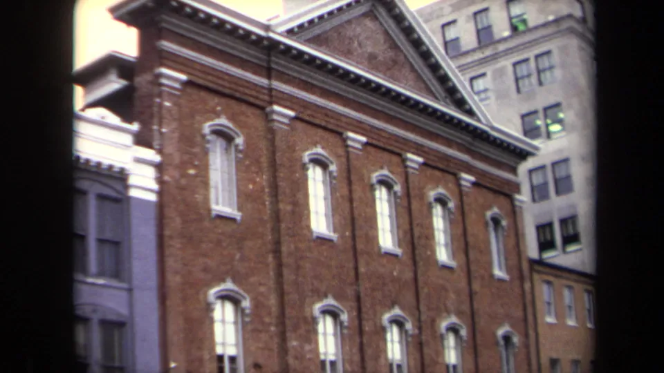Vintage 8mm frame of Ford's Theatre from an angled Washington, DC street view, with arched windows and neighboring facades visible.