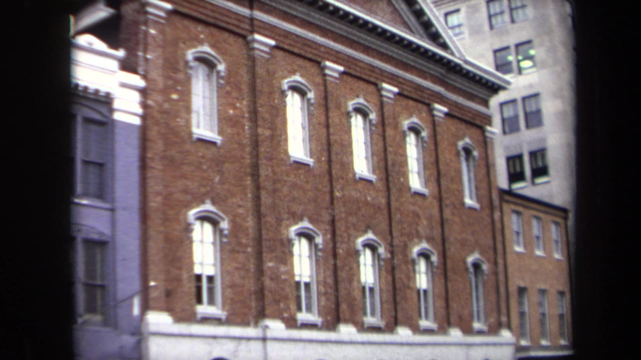 1970 Washington, DC home-movie frame showing a red brick urban building facade with white-trimmed windows and adjacent city structures.