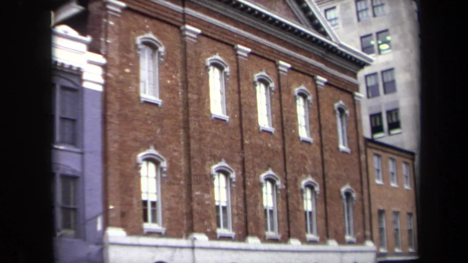 1970 Washington, DC home-movie frame showing a red brick urban building facade with white-trimmed windows and adjacent city structures.