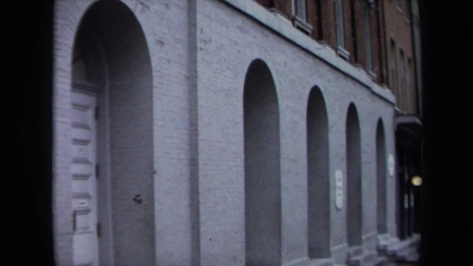 1970 Washington, DC home-movie frame with a closer, slightly blurred view of arched ground-floor openings on an urban brick building.
