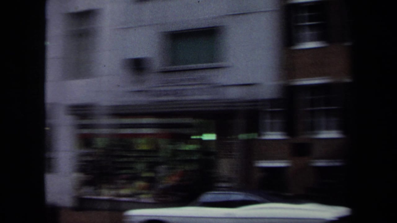 1970 Washington, DC street view with motion-blurred storefronts, brick buildings, and a light-colored parked car at curbside.