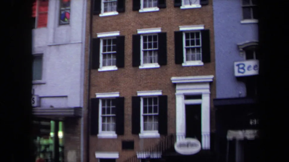 1970 Washington, DC rowhouse facade with black shutters, white doorway trim, neighboring shopfronts, and partial Beef signage.