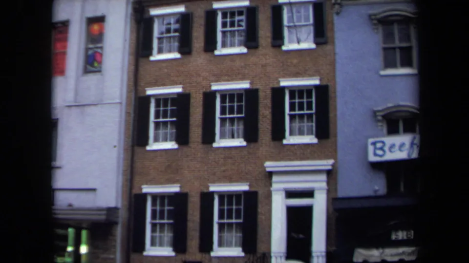 1970 Washington, DC townhouse exterior showing a brick facade, black shutters, white entry surround, and neighboring business signage.