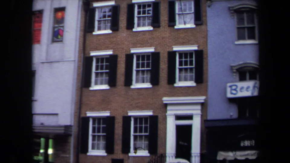 1970 Washington, DC exterior of a brick rowhouse with shuttered windows, white trim, adjoining storefronts, and partial Beef signage.