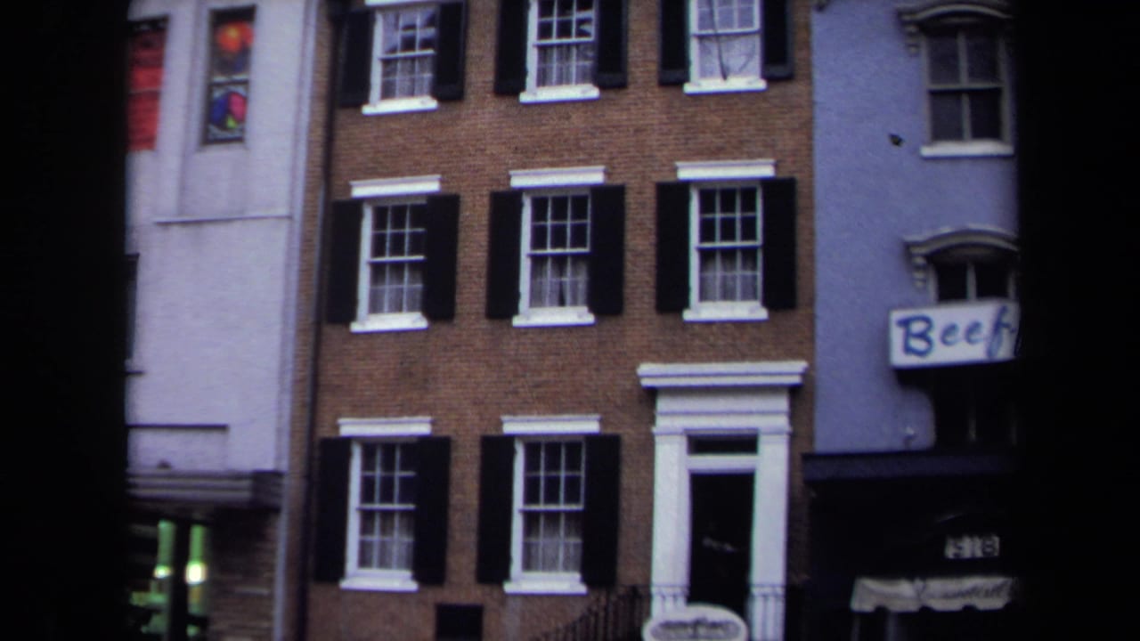 1970 Washington, DC home-movie frame showing a brick townhouse facade with black shutters, white trim, and adjacent buildings.