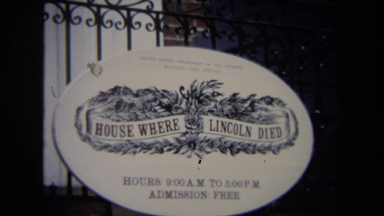 1970 Washington, DC home-movie frame of the oval House Where Lincoln Died sign with posted visitor hours behind an iron fence.