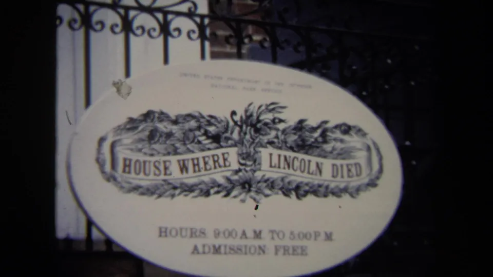 1970 Washington, DC home-movie frame of the oval House Where Lincoln Died sign with posted visitor hours behind an iron fence.