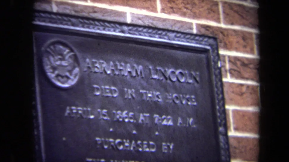 Close 1970 Washington, DC home-movie frame of the Abraham Lincoln memorial plaque with raised lettering on a brick wall.