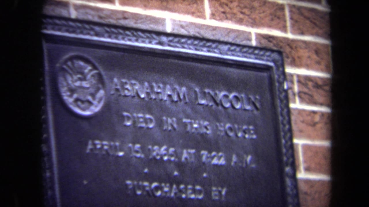 1970 Washington, DC 8mm frame showing a dark metal plaque about Abraham Lincoln's death mounted against brick.