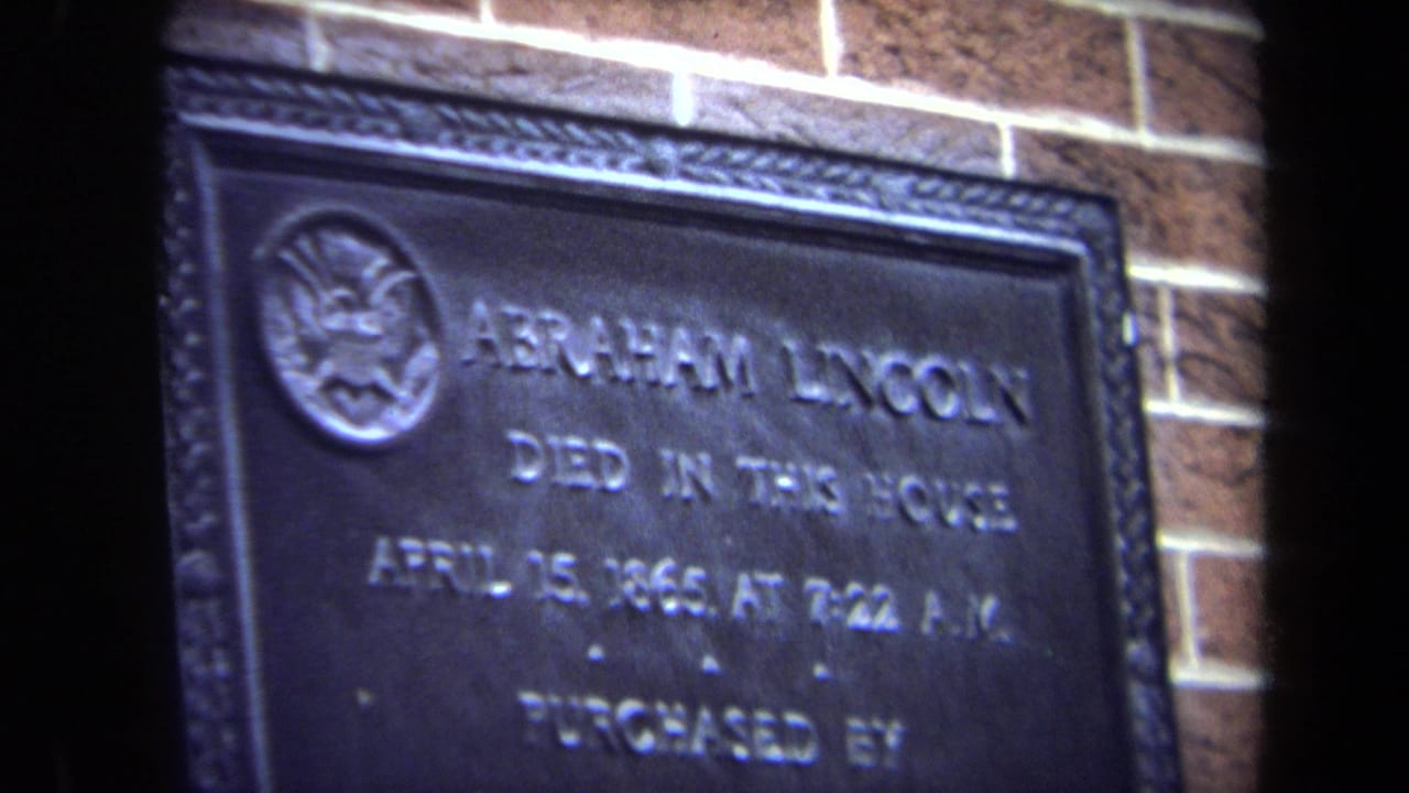 Dark metal plaque with Abraham Lincoln lettering and brick wall behind it.