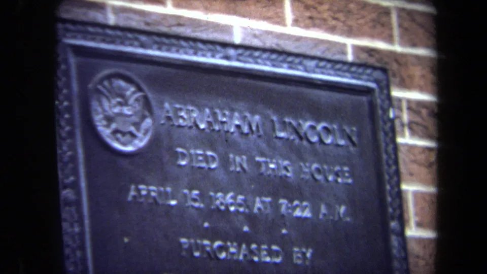 1970 8mm frame with a slightly tilted close view of the Abraham Lincoln plaque and its raised inscription on brick.