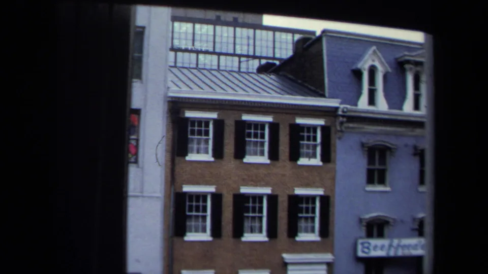 Washington, DC rowhouse facade with brick walls, black shutters, white-trimmed windows, dormers, and partial storefront signage.