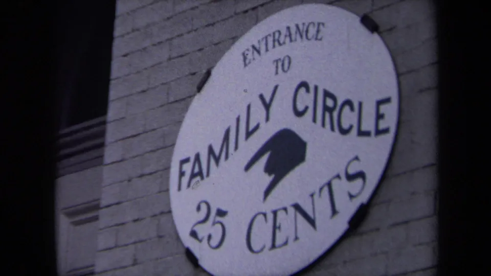 Handheld close-up of the Family Circle 25 Cents entrance sign, with brick texture and dark film-edge shadow visible.