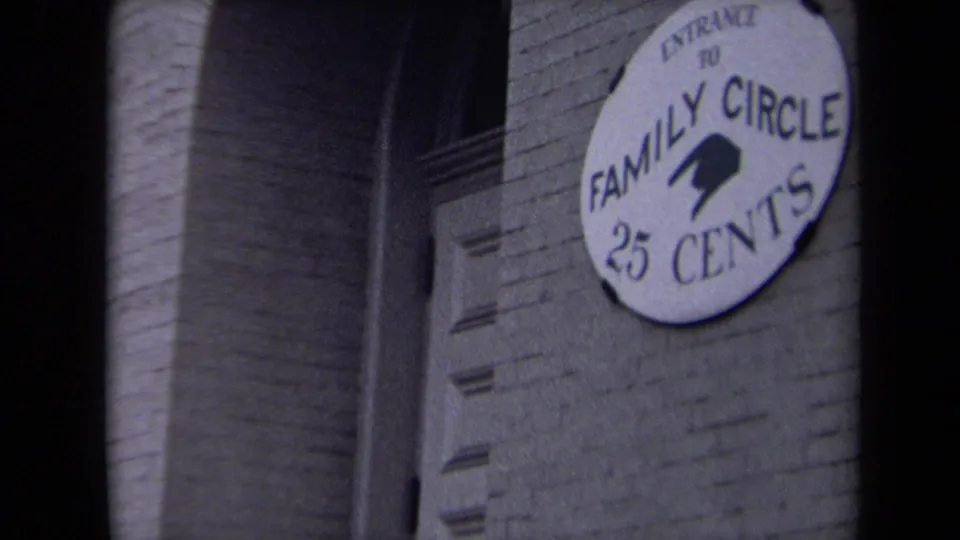 Washington, DC home-movie frame showing the Family Circle 25 Cents sign beside brick masonry and a recessed doorway or opening.