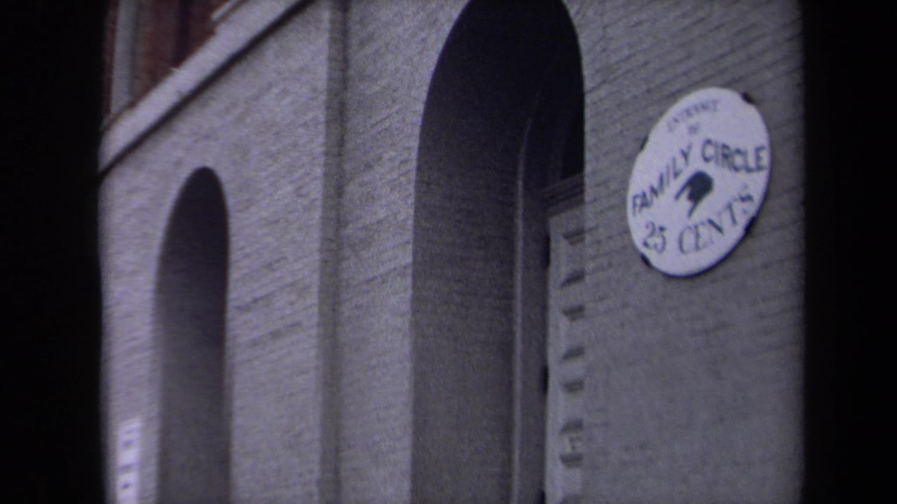 1970 Washington, DC home-movie frame showing a brick theatre facade with arched openings and a round Family Circle 25 Cents sign.