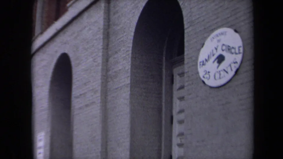 1970 Washington, DC home-movie frame showing a brick theatre facade with arched openings and a round Family Circle 25 Cents sign.